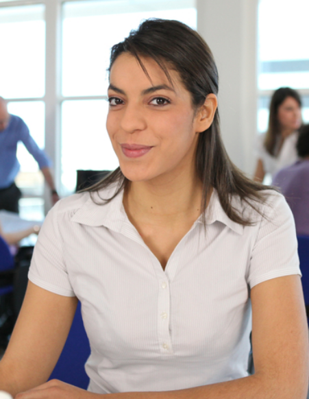 Confident woman, seated at a desk, gazes directly at the camera.